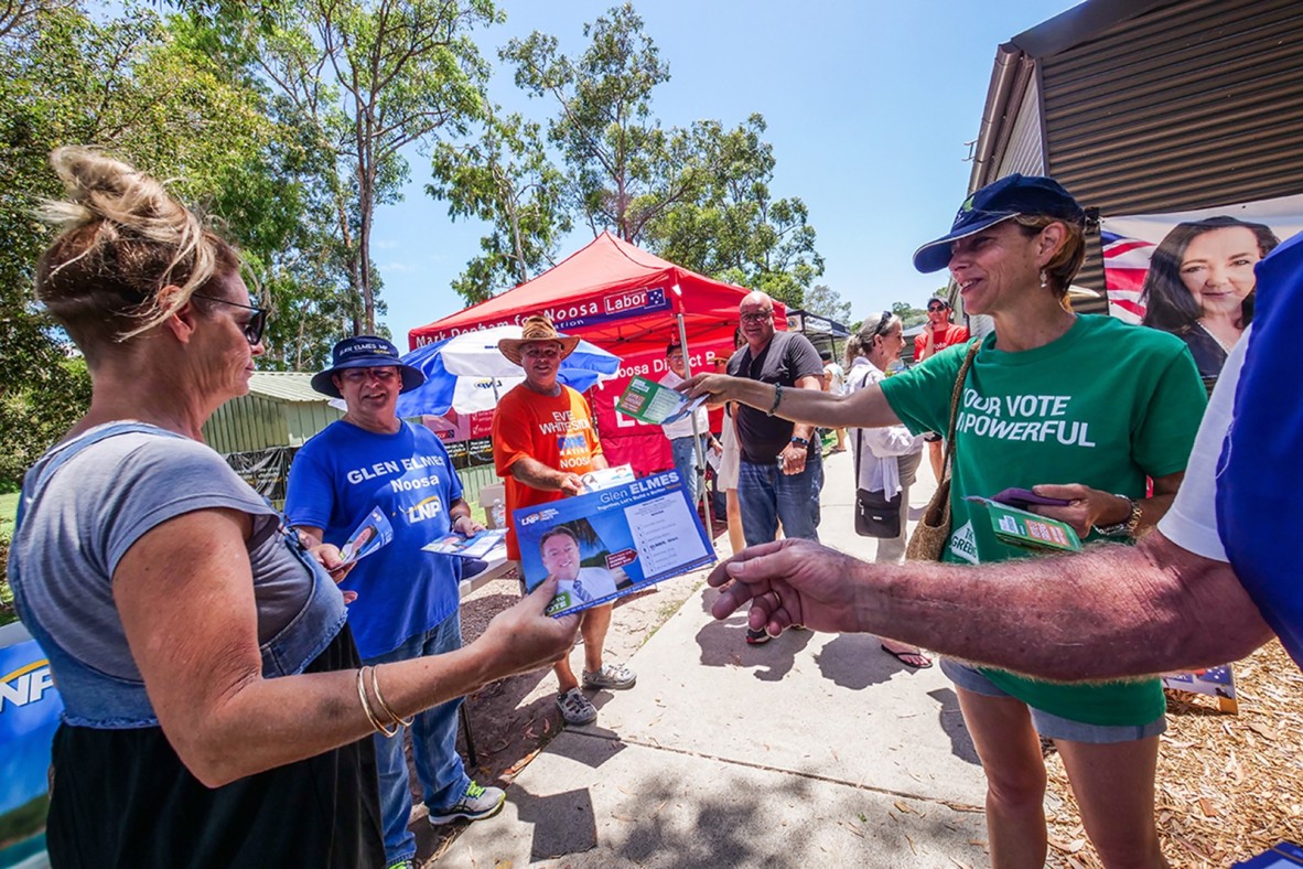 A woman is walking into the polling centre at Sunshine Beach. She is presented with how-to-vote cards by volunteers from the Australian Labor Party, the Library National Party and The Greens.