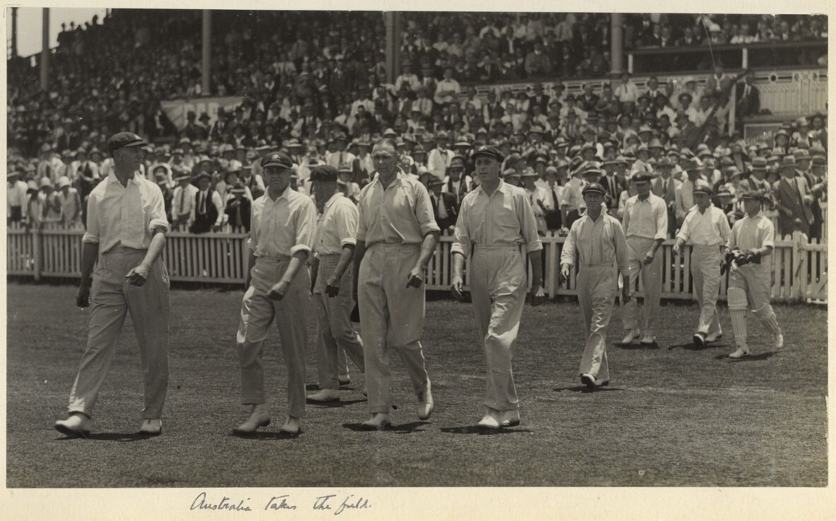 Cricket players on the Australian team walk out in front of the Exhibition Grounds' grandstand.