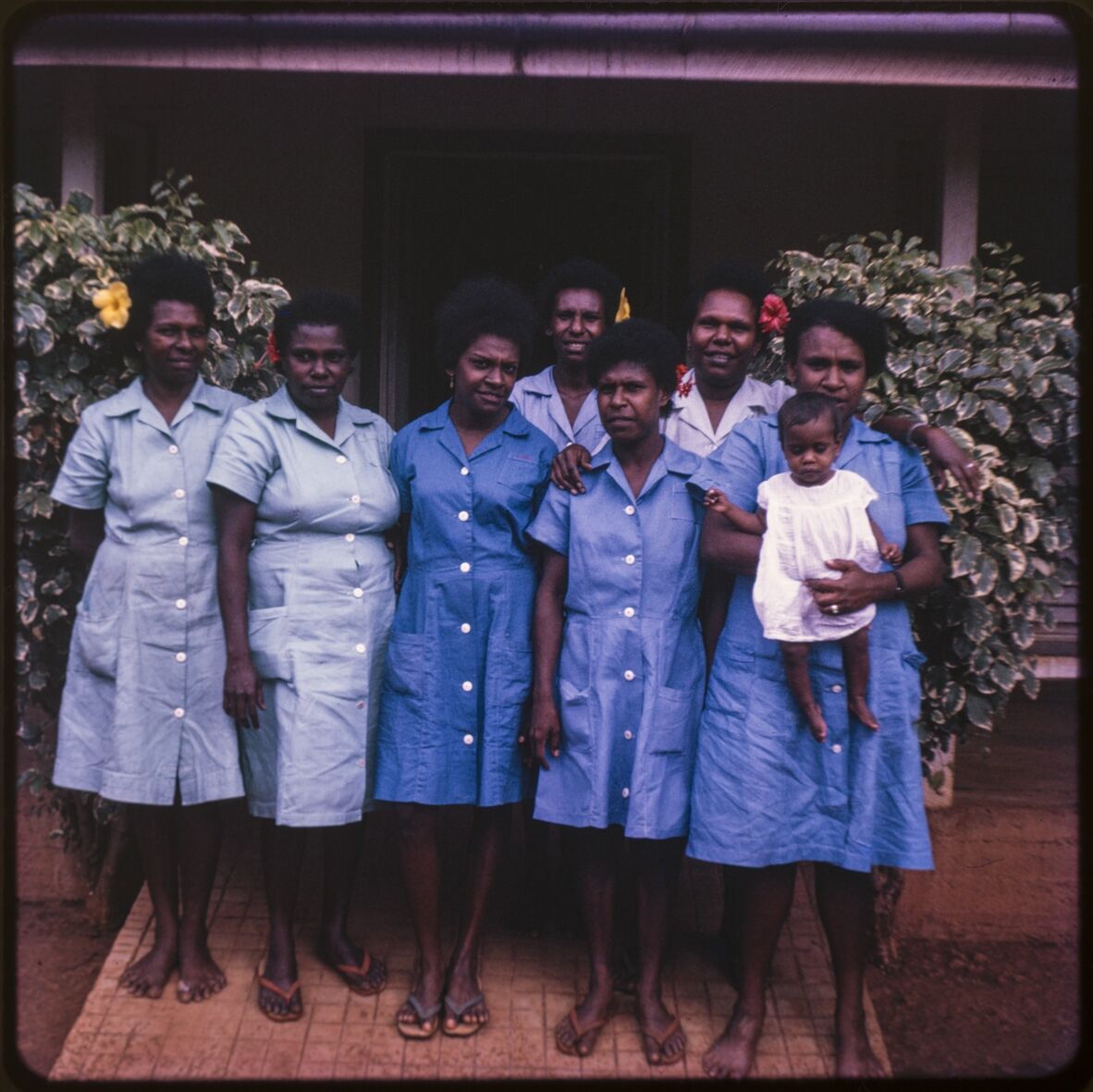 A group of seven Torres Strait Islander nurses pose for a photograph with a toddler