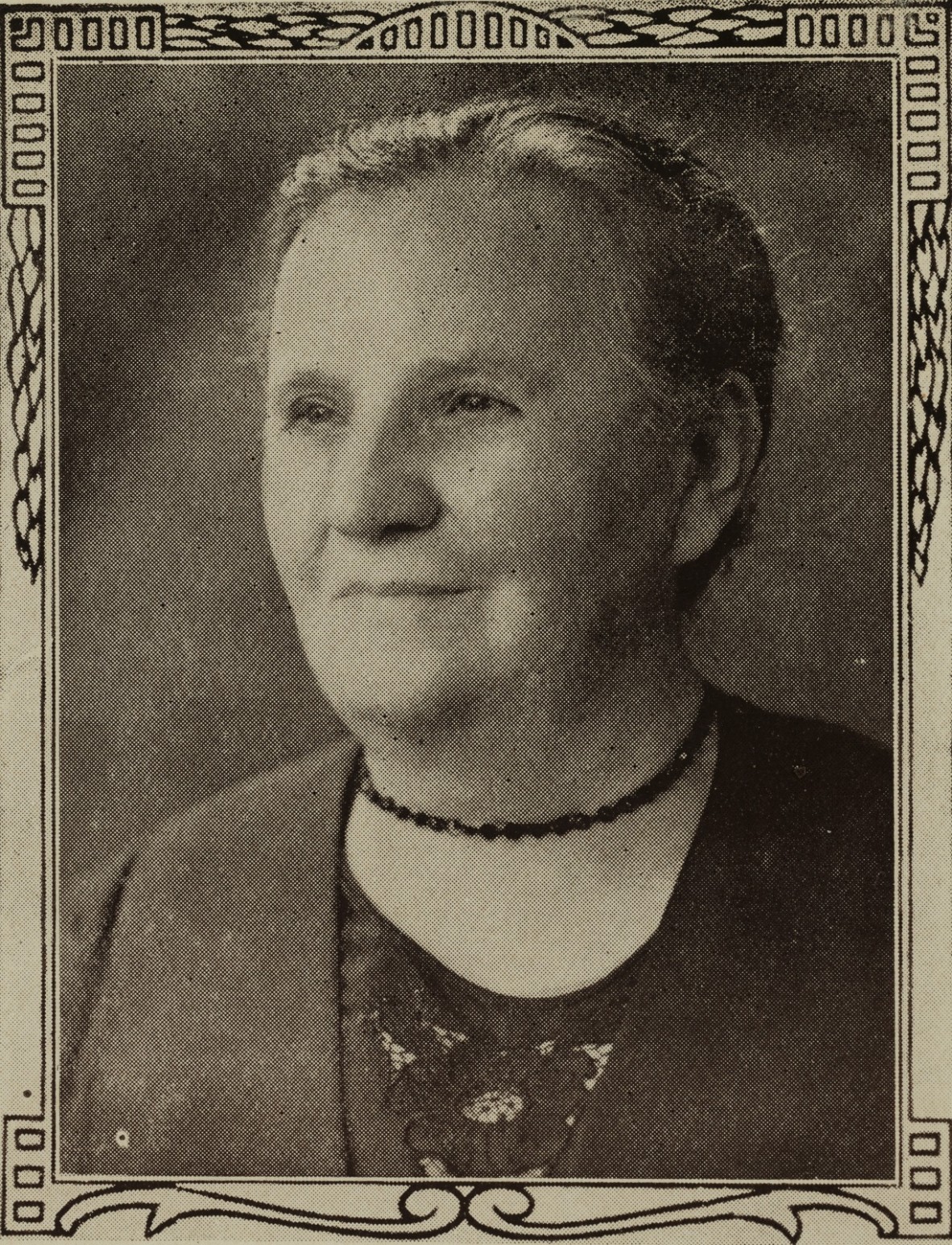 A black and white photograph of an older white woman in a blazer, black necklace with tied back hair.
