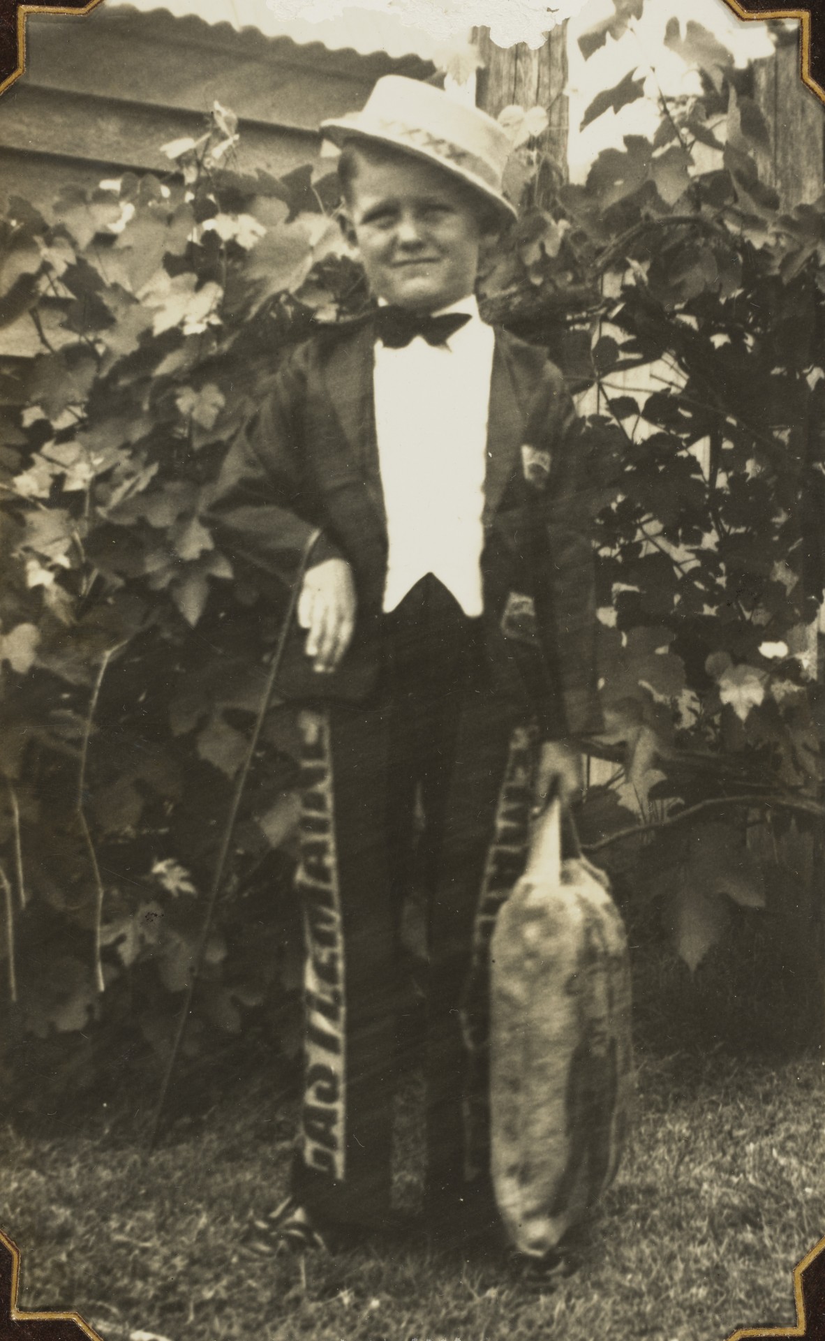Black and white photograph of a young boy dressed as 'Mr Fourex', with a straw hat, tuxedo and cane.