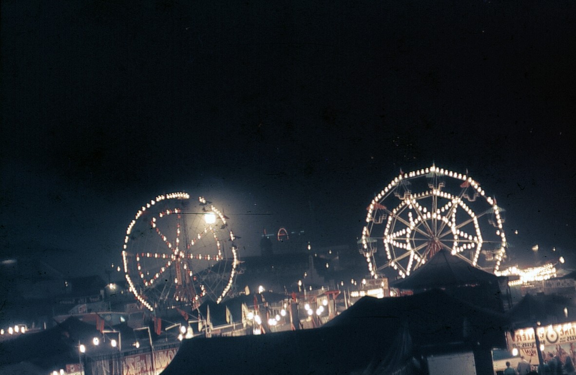 Ferris wheels at night during the Ekka at the RNA showgrounds, Brisbane, August 1963