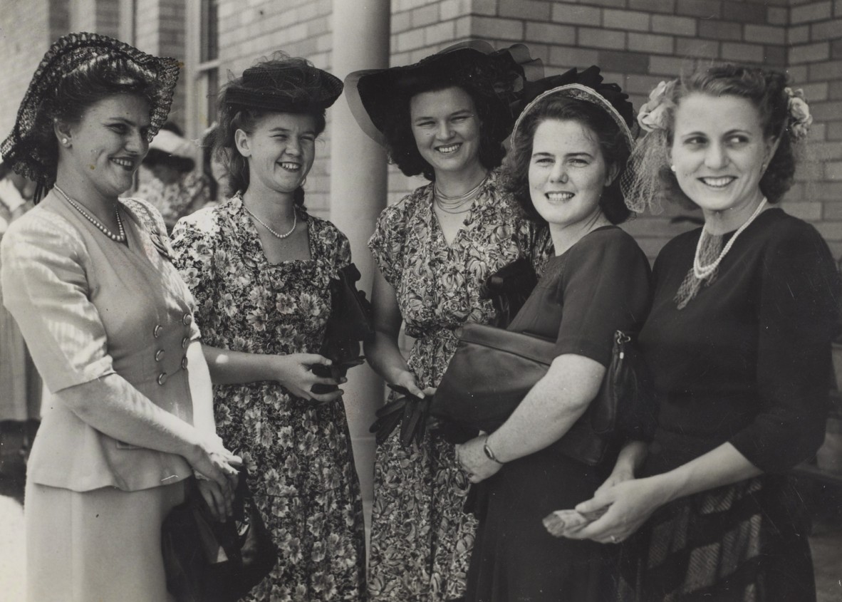 Old photograph of a group of women wearing dresses and ornate hats.
