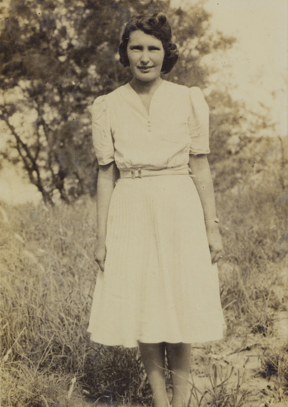 Sepia image of a woman in a white dress standing in grass with tree behind