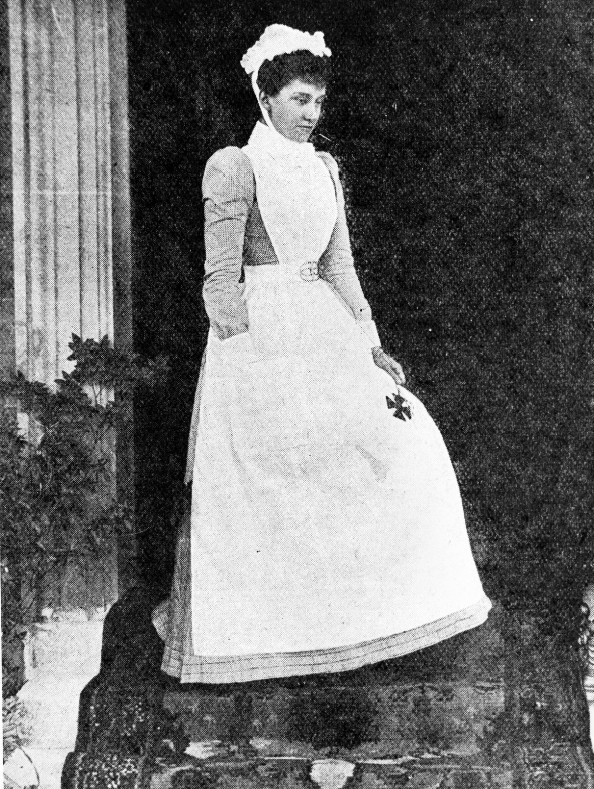 Black and white photograph of a woman dressed in a nurse's uniform typical of the late 1890s..