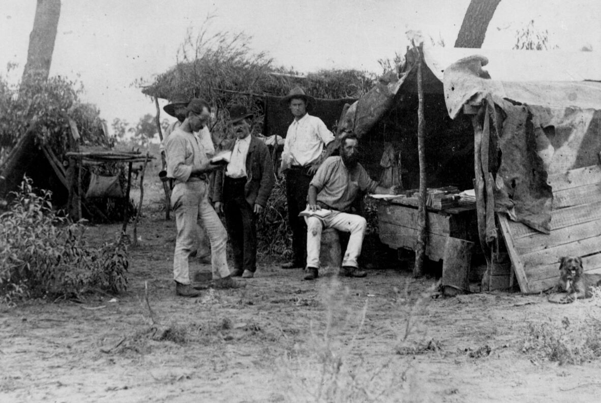A black and white photograph showing five men standing and sitting near makeshift lodgings during the Barcaldine Shearer's Strike in 1891.