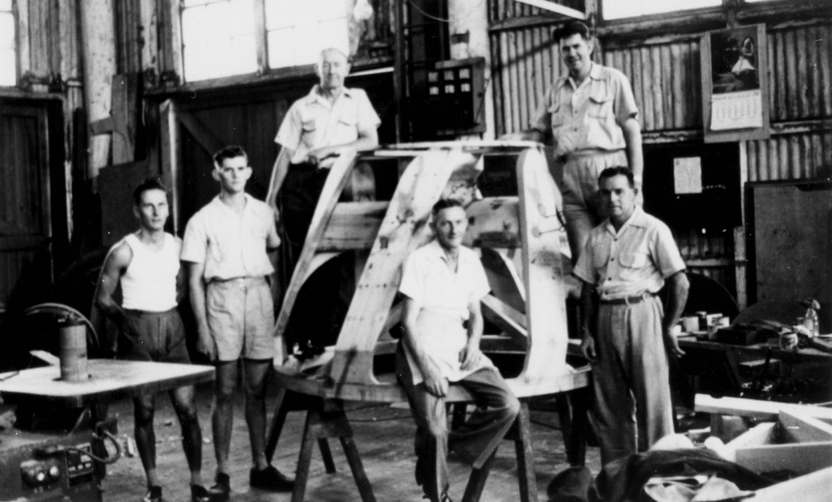 Old photograph of men standing around a metal structure in a factory.