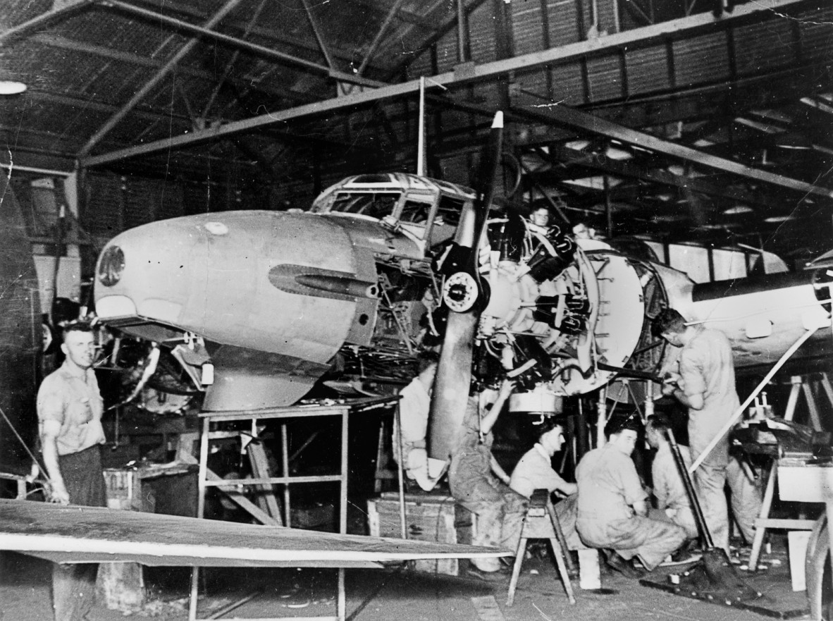 Old photograph of mechanics working on a disassembled plane.