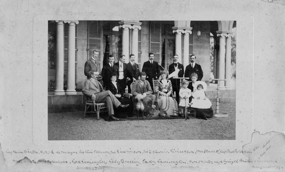 A black and white photograph of men, women and children sitting and standing outside Government House, Brisbane.