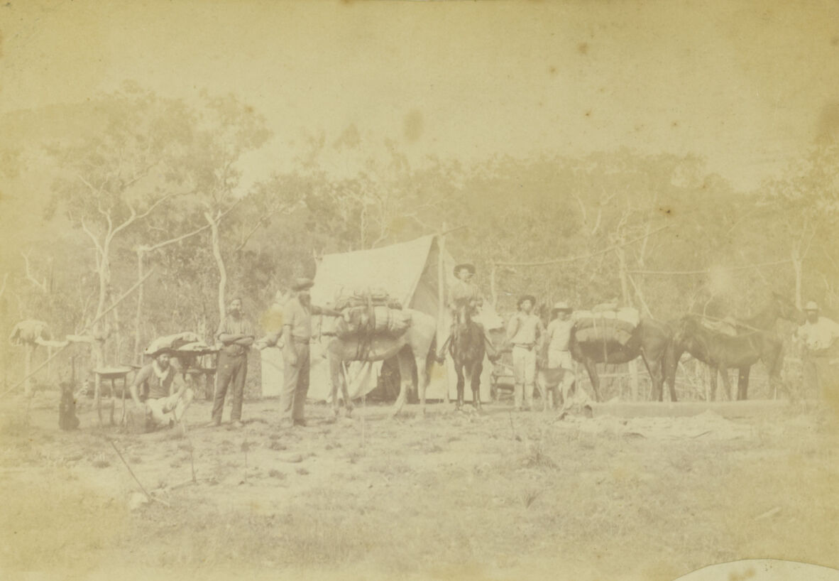 A faded black and white photo showing men in a bush camp with tents and horses
