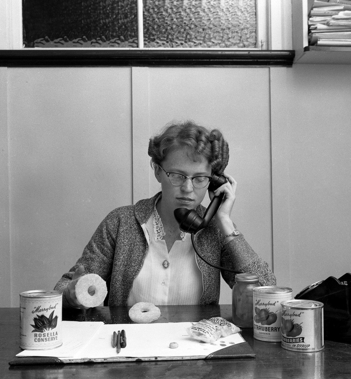 Photo of business woman sitting at a desk on the phone, with 3 tins of jam on the desk