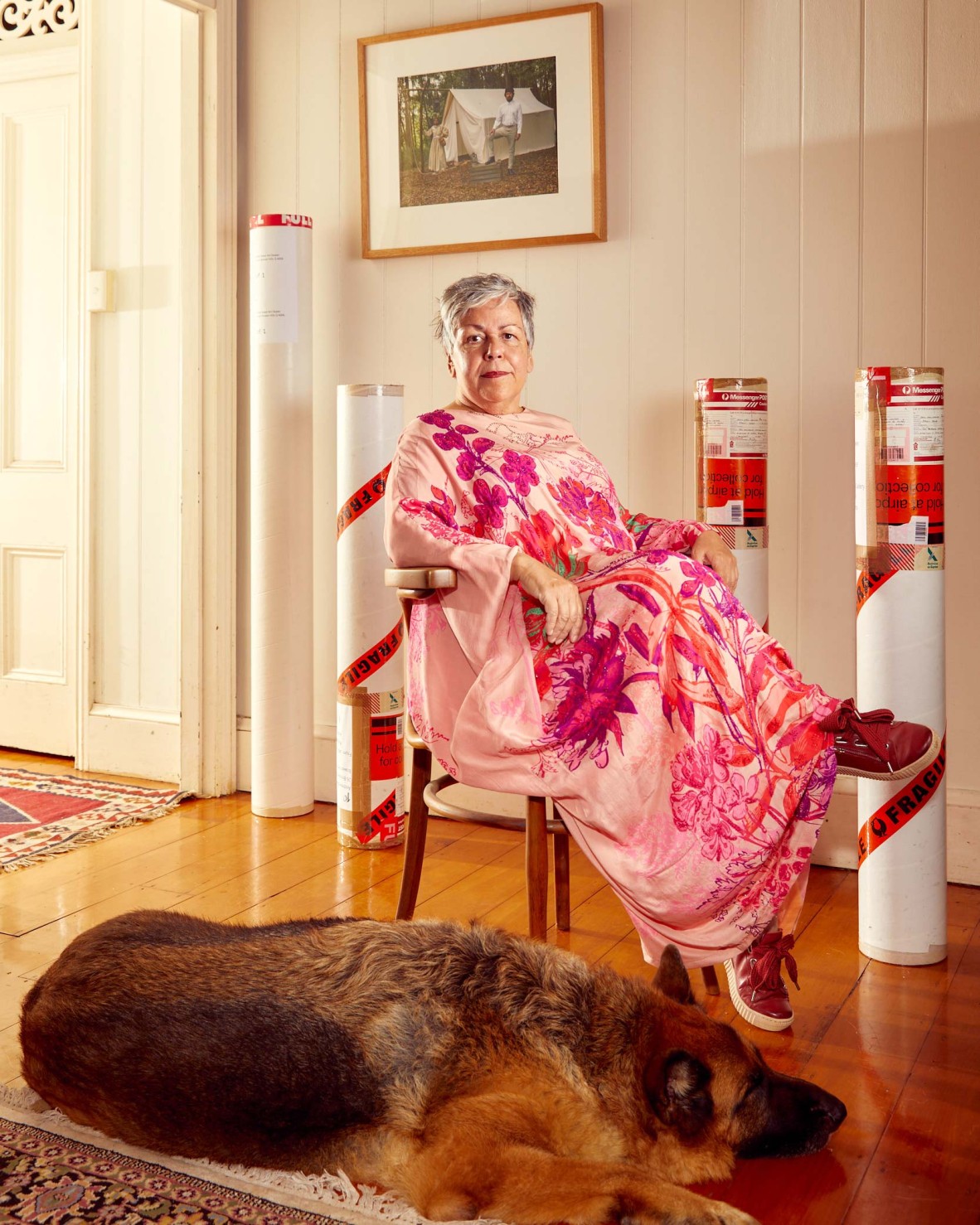woman in colourful pink flowered dress sitting on chair with large dog resting on floor