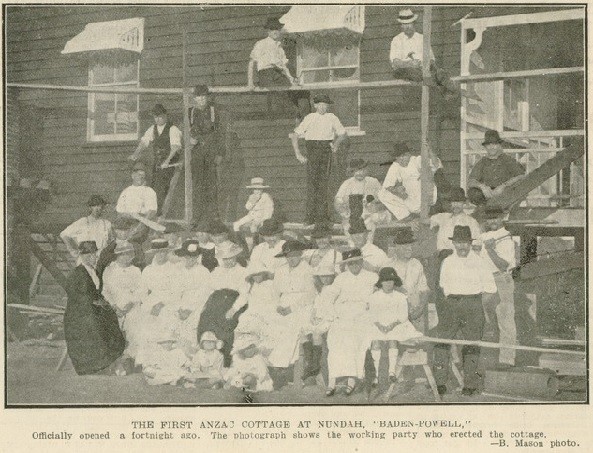 Group of people sitting in front of side wall of house, 1919