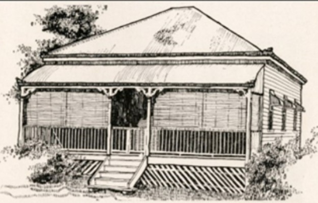 A small house with pointy roof surrounded by bushes and a tree