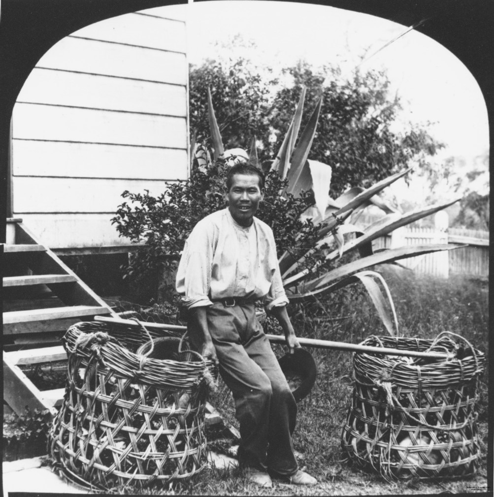 A picture of a man sitting down with two baskets of fruit and vegetables