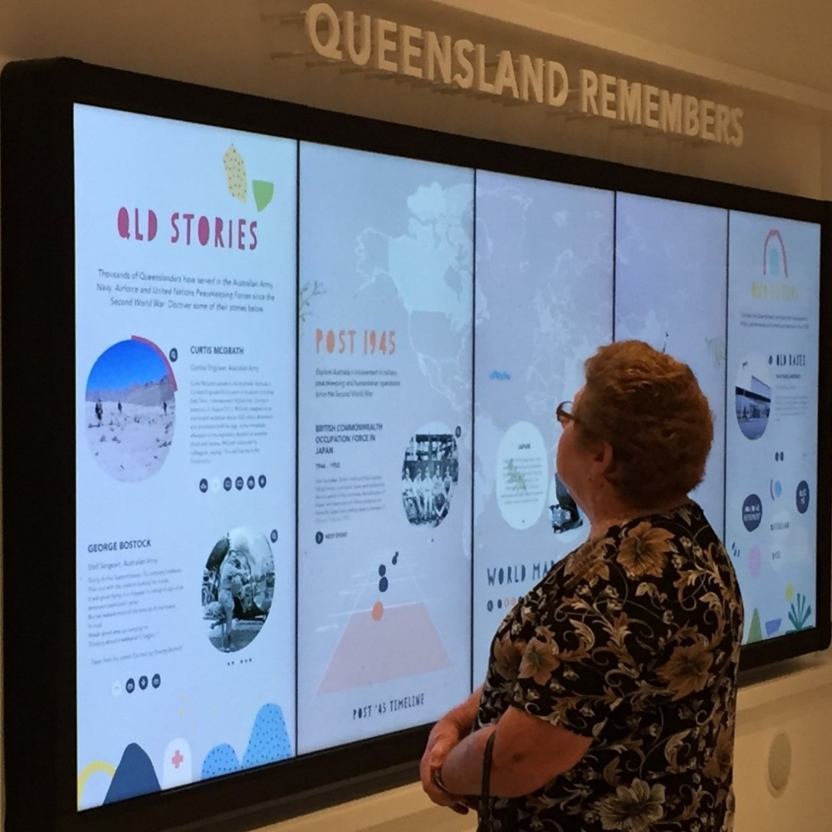 Woman standing in front of Queensland Stories display in Post 1945 Gallery at Anzac Square Memorial Galleries