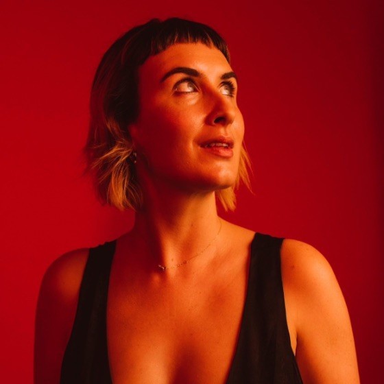 Grace McCarter wears a black top and looks away from the camera, against a red background