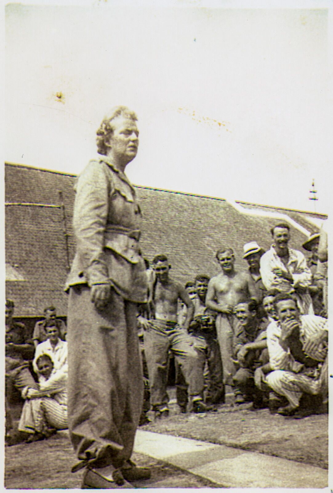 Gracie Fields is dressed in military uniform with patients grouped around her as she sings to them in Tarakan, Borneo.
