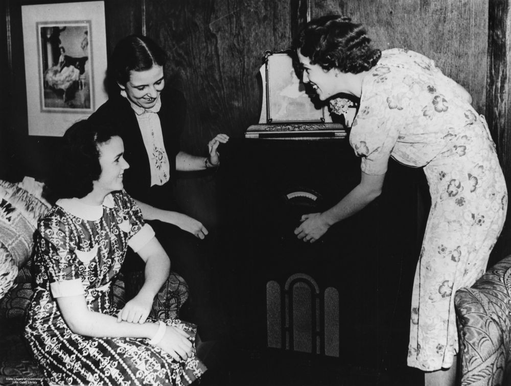 Three women gathered around a radio