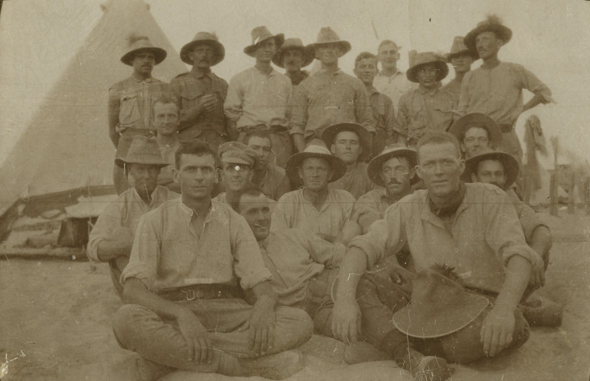 Group of soldiers seated and standing in sand at military camp in Eygpt, 1918.