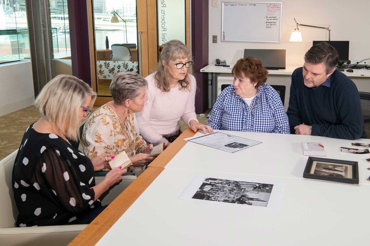 Group of 4 women and man sitting at table looking at photos and documents