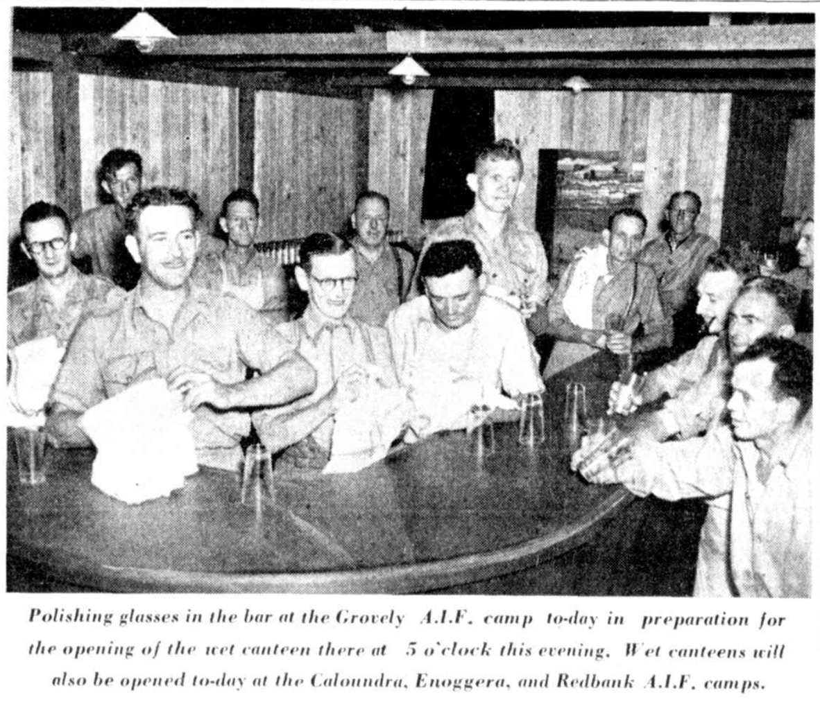 An archival, black-and-white newspaper clipping showing several men in military uniform standing behind and around a curved wooden bar inside a rustic canteen with wooden-paneled walls and hanging light fixtures. Several men in the foreground are actively polishing glasses with white cloths.