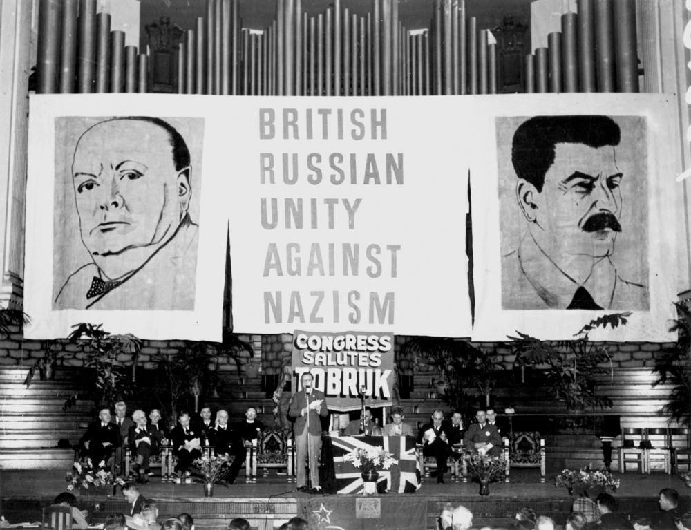 Guests seated on stage in front of a backdrop of giant posters at the Aid to Soviet Congress Brisbane City Hall October 1941