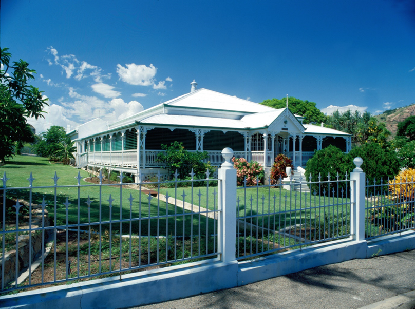 A colour picture of a white house and fence with green lawn and flowers