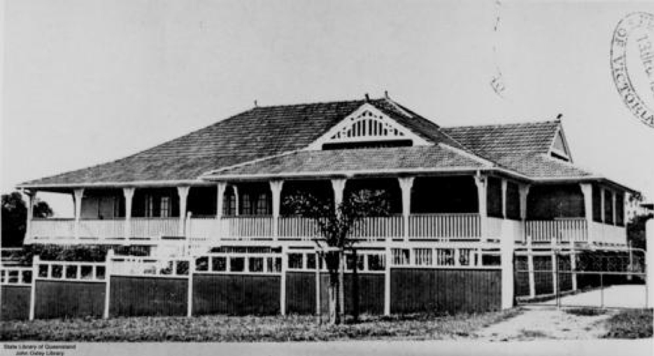 A black and white picture of a house with a wide verandah and prominent front fence in