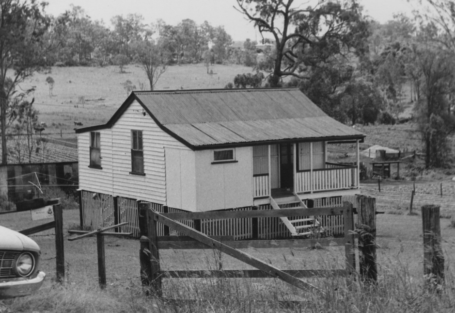 A black and white photograph of a house with a raised verandah M roof and the corner of a car parked out front at Mtichelton