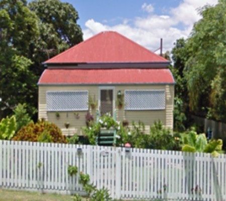 A cream coloured house with a red roof and white picket fence