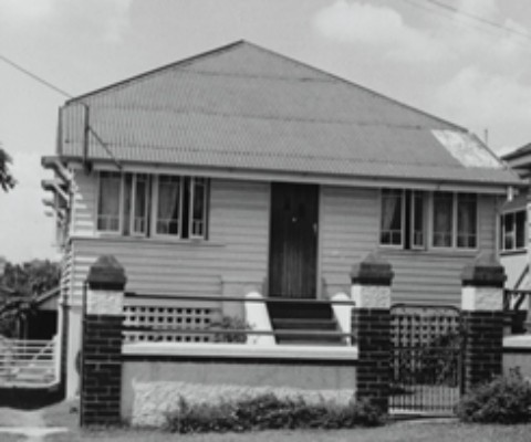 Photograph of a weatherboard house with brick columns and a gate at the front