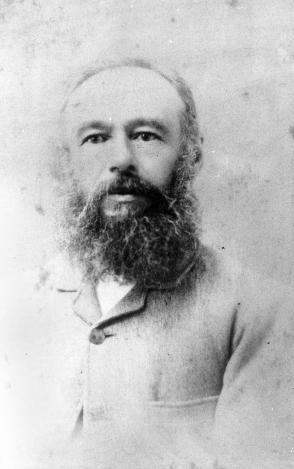 Black and white portrait of Gustav Adolph Riebe, ca. 1890, wearing a buttoned up jacket and a bushy beard.