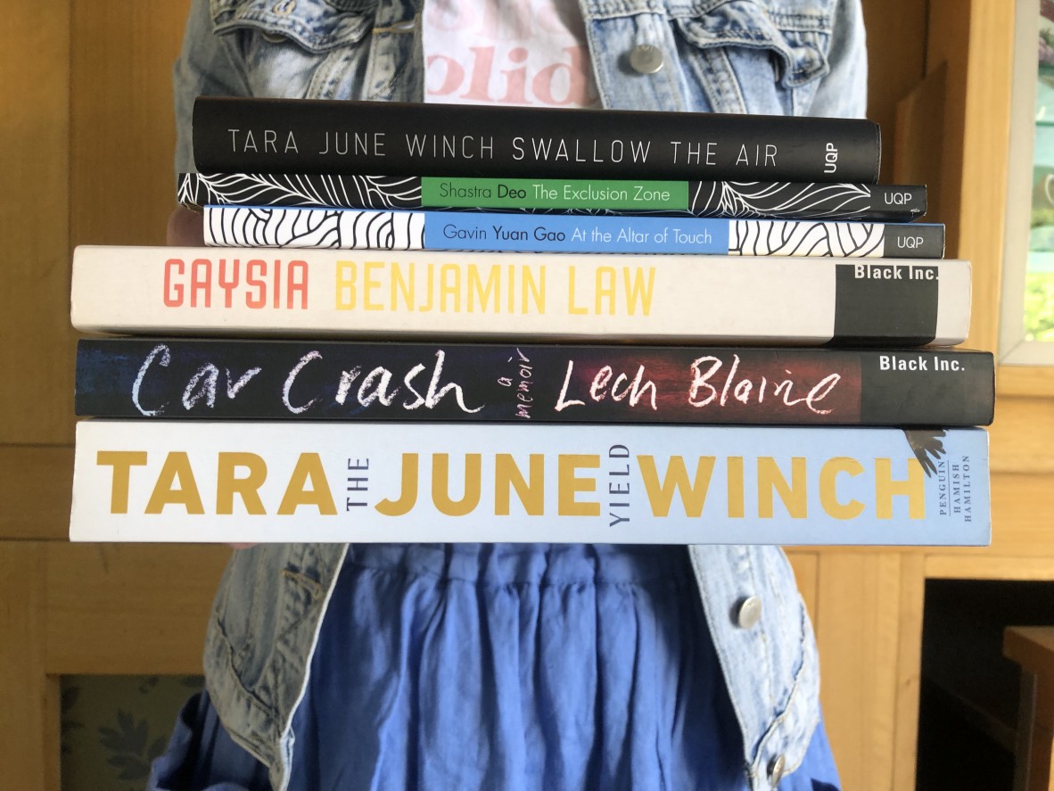 A person is holding a stack of books including 'Swallow the air', 'The exclusion zone', 'At the altar of touch', 'Gaysia', 'Car crash', and 'The yield'
