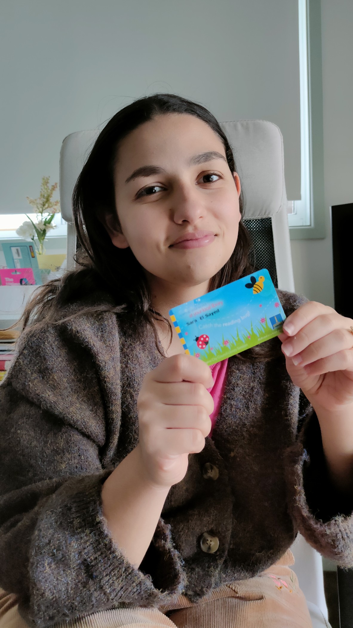 Sara El Sayed holds her Brisbane City Council library card It is blue with a bee and a ladybird