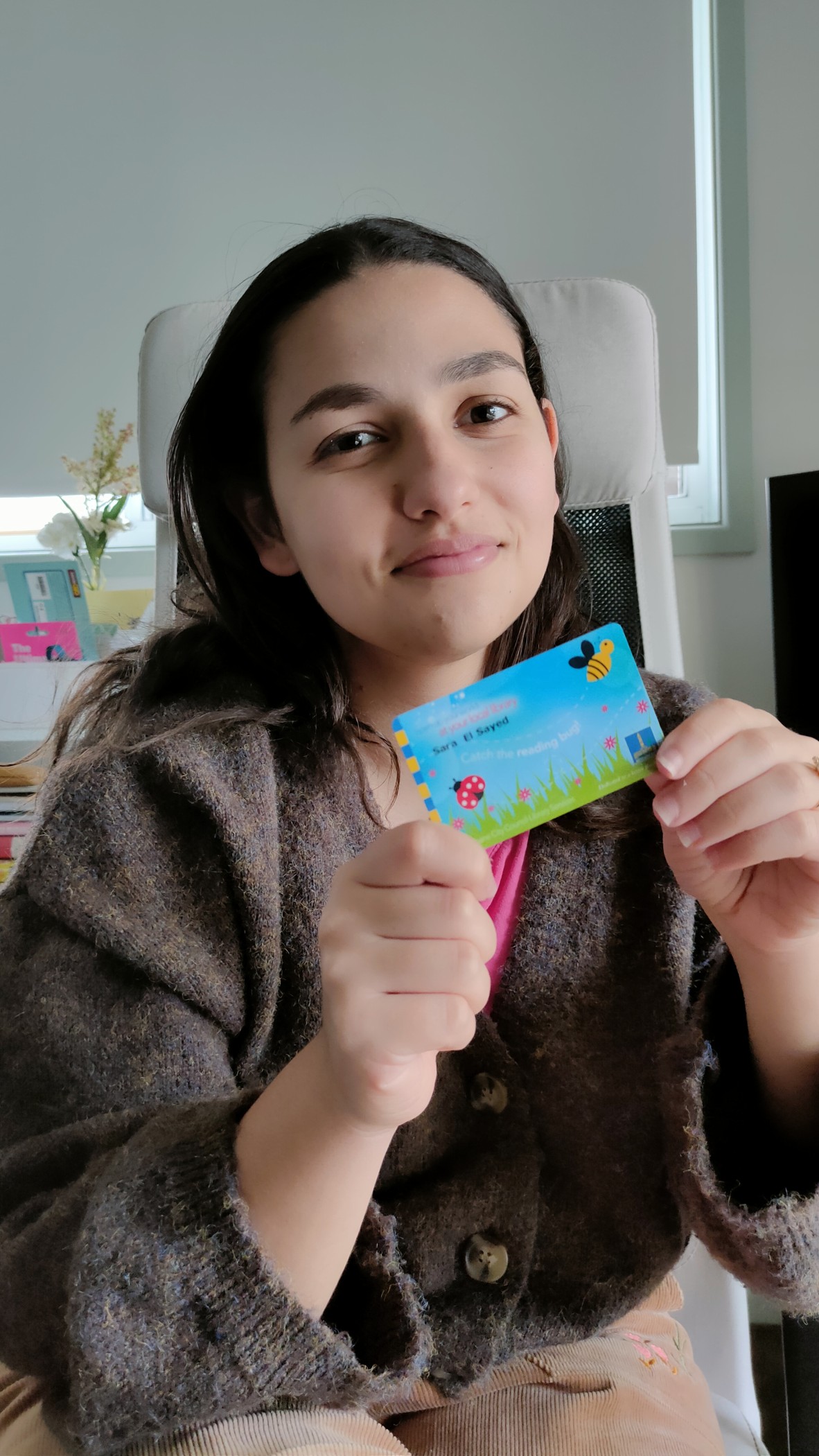 Sara El Sayed holds her Brisbane City Council library card. It is blue with a bee and a ladybird.