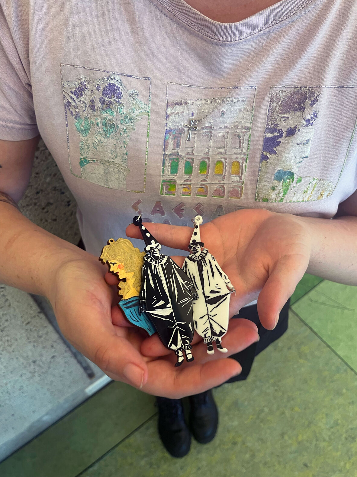 Close up photo of a young women in purple holding a few laser cut items. One is in the shape of a women's bust and has being coloured in, and then the other two are in the shape of a clown, with one being black and one being white.