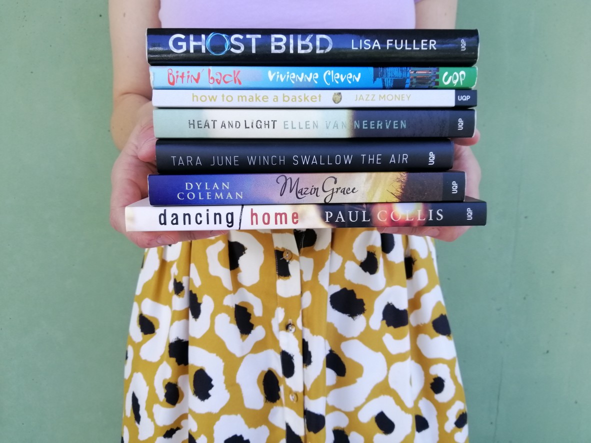 A person in a purple top holds a stack of books against a green background
