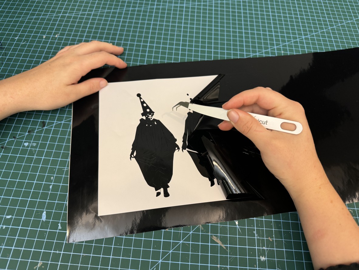 a photo of hands weeding out a vinyl sticker of a small cut out clown.