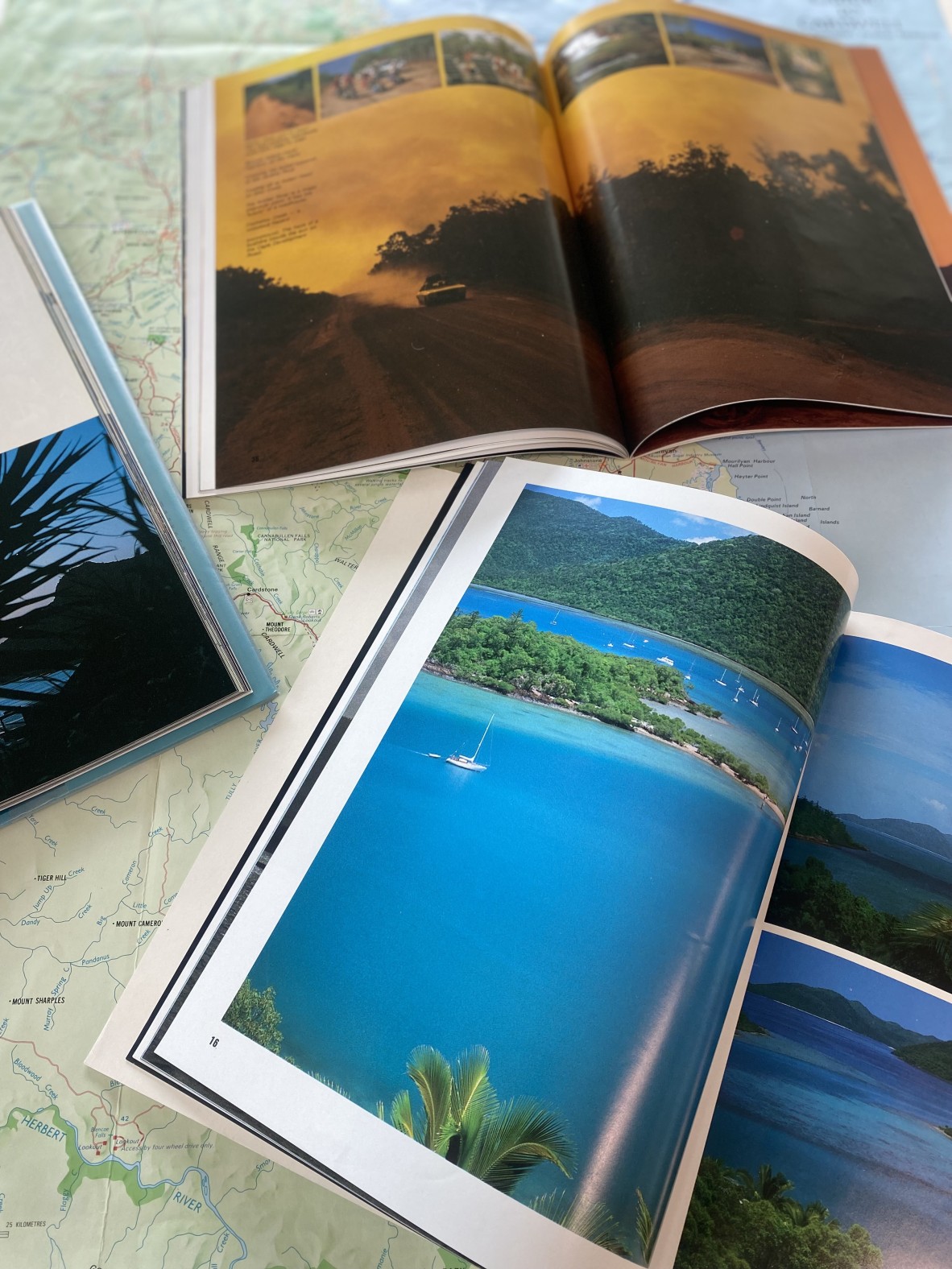 three tourism books a bay and land, and a car driving through dust in a bushfire haze