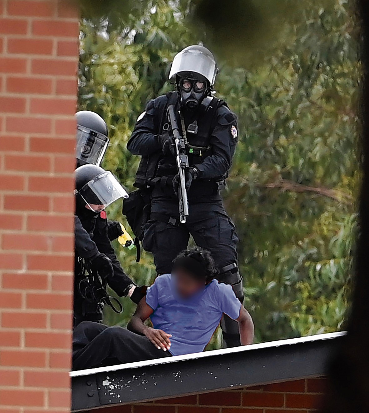 A photo of prison officers pointing a gun at a teenager whose face is blurred out for privacy