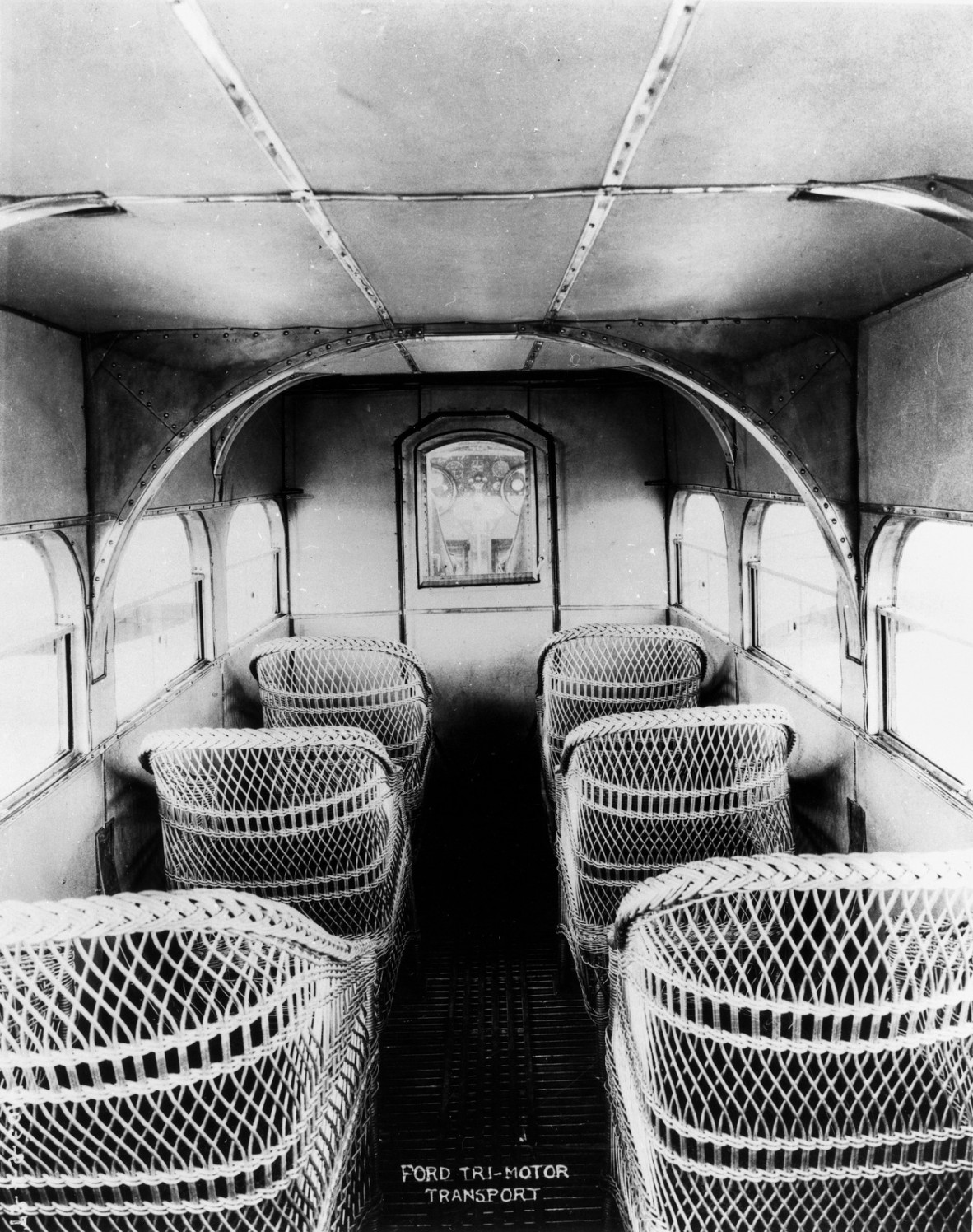 Interior of the Ford Tri-Motor Transport, ca. 1925 Cane seating in the cabin of the transport aeroplane. The instruments of the cockpit can be seen through the connecting door. Cane seating was light.
