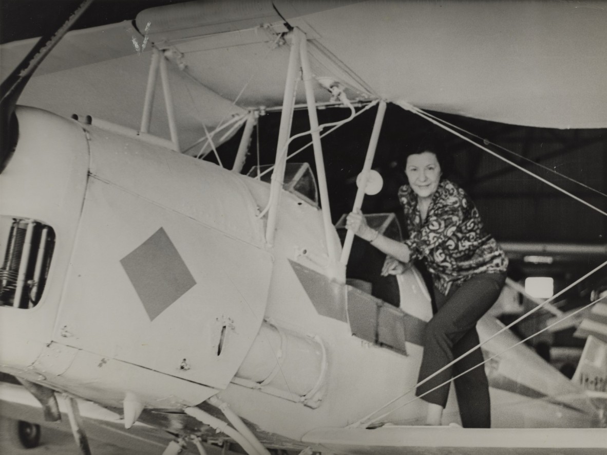 a woman is posing for a photo standing on the wing of a light aircraft