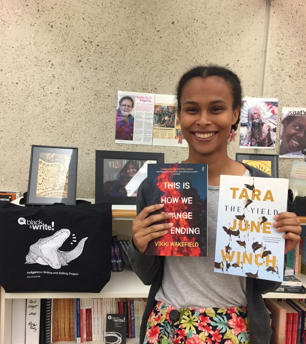 Jasmin McGaughey stands against a bookshelf, holding up a Vikki Wakefield book and a Tara June Winch book