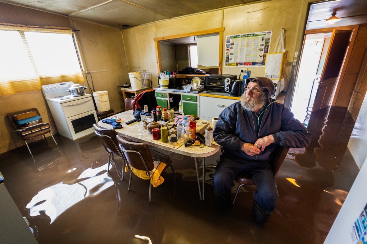 A man sitting in a flooded kitchen at a table in calf-high water