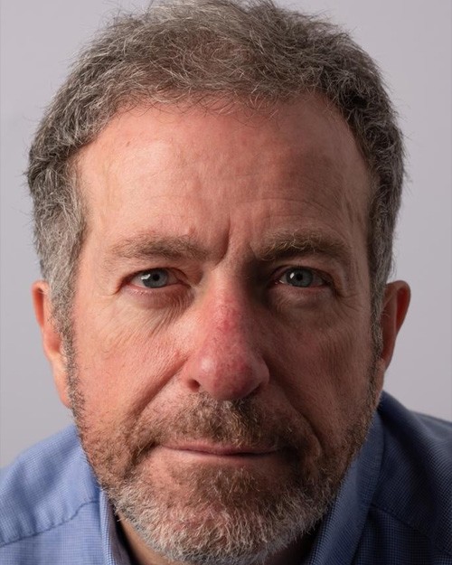 Headshot of John Richards; a close up image – John is wearing a blue button up shirt. He has a light beard and blue eyes