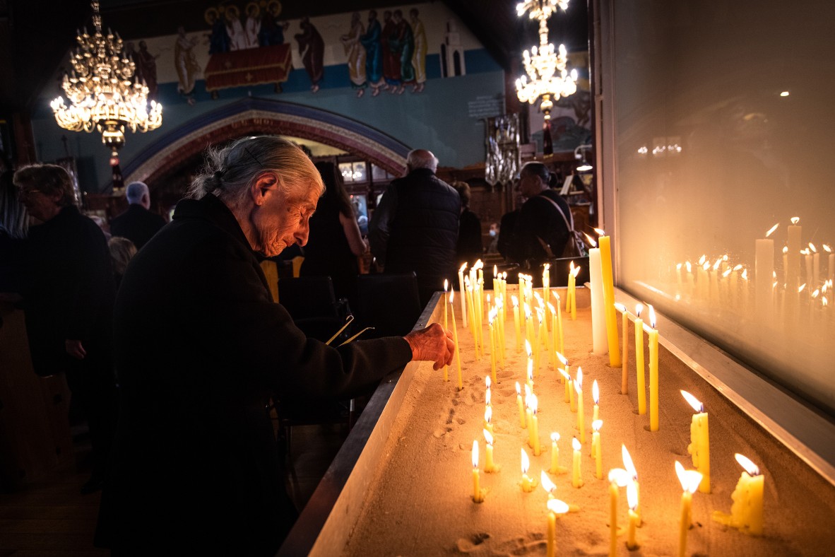 An elderly woman lights candles at a funeral service