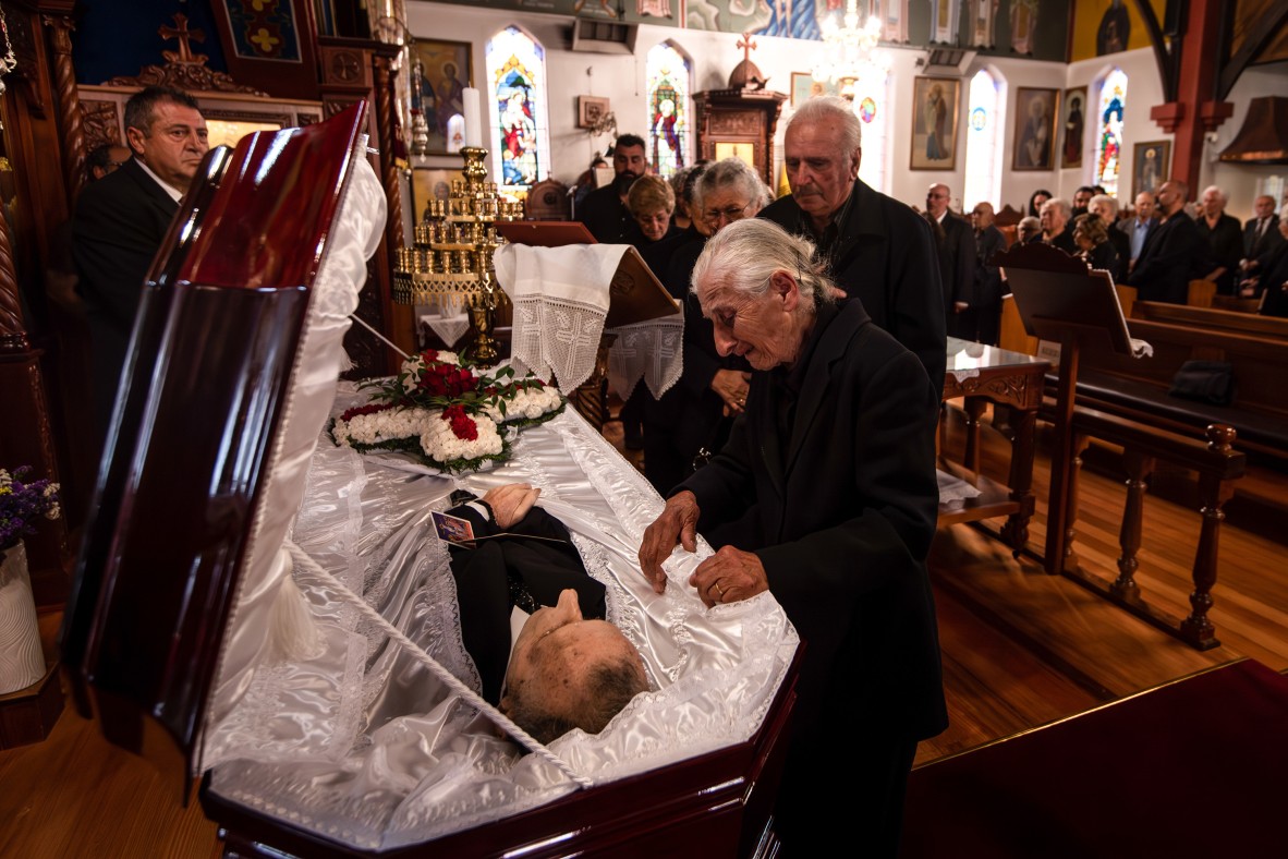 An elderly woman mourns her husband in a casket at a funeral service