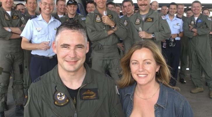 Man in flight uniform standing with woman in front of a group of people in defence uniforms