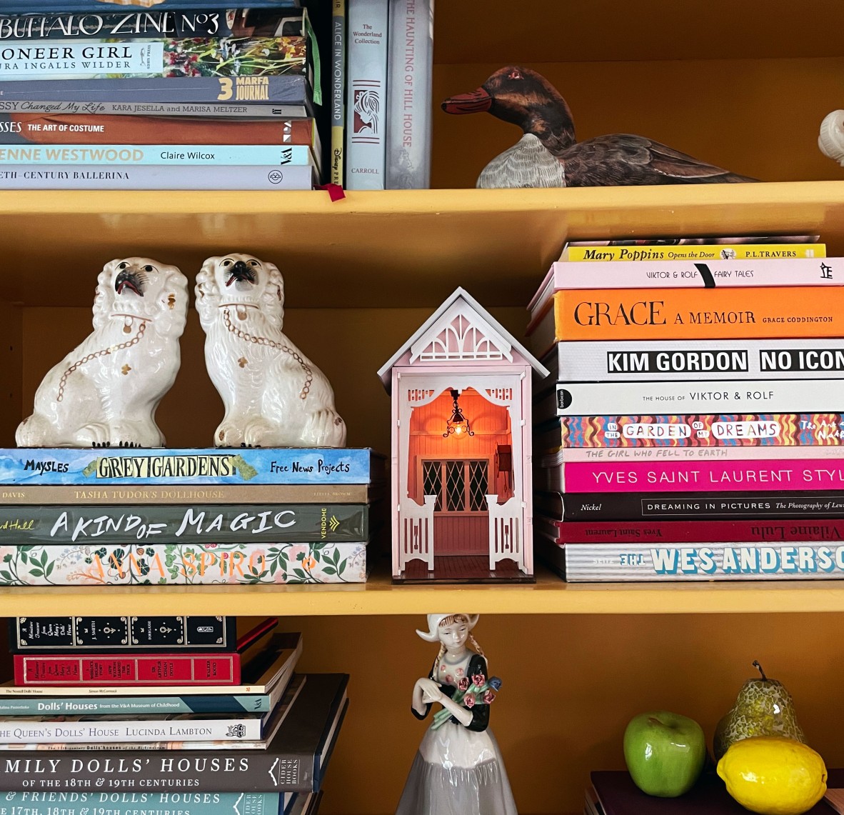 A pink book nook with white accents sitting in between a bunch of books on a bookcase.